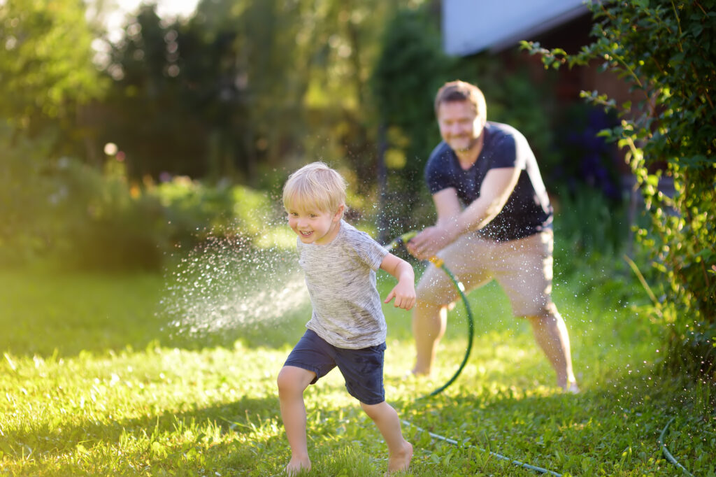 Little boy getting sprayed by his father with a hose because their plumbing works.