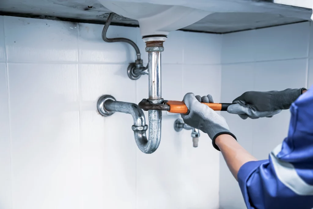 plumber tightens loose pipes under sink with wrench