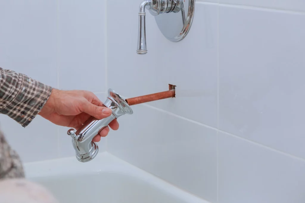 man inspects and cleans old bathtub faucet area before replacing