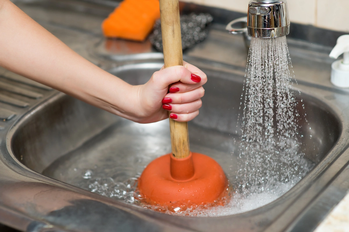 woman unclogs drain with plunger