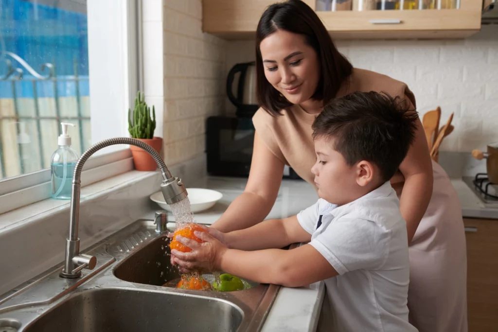 woman helping her son washing the fruits under tap water