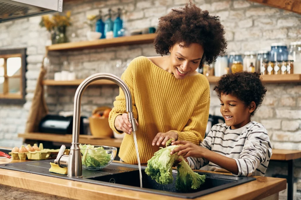 parent and child washing vegetables on kitchen sink