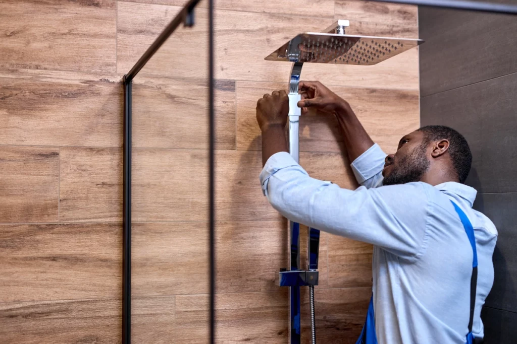man installing a shower head in wood siding bathroom
